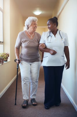 A senior woman walking with a nurse in a hallway