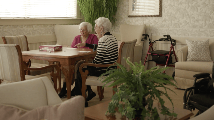 Two elderly women playing a board game in a common area