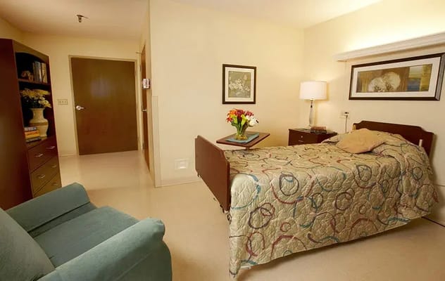 A cozy private bedroom with a bed, lamp, and bookshelf.
