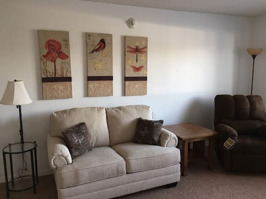 A comfortable living room with a beige sofa, decorative artwork, and a lamp.