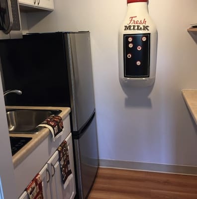 Compact kitchenette with stainless steel refrigerator and decorative milk bottle dispenser