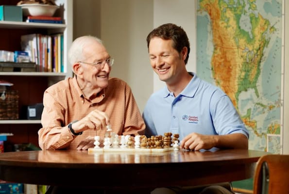 An elderly man playing chess with a caregiver.