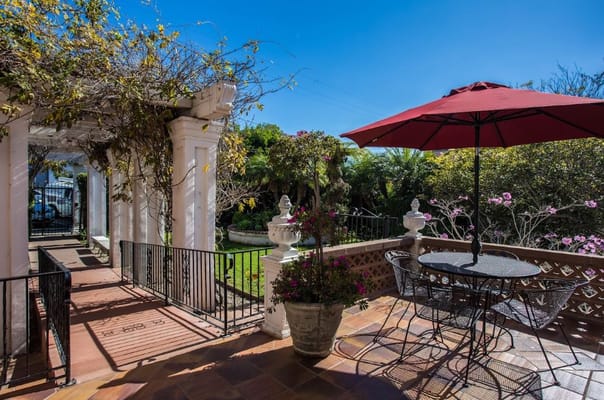 A sunny patio with a table and umbrella surrounded by greenery