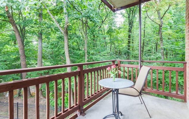 Balcony with a table and chair overlooking green trees