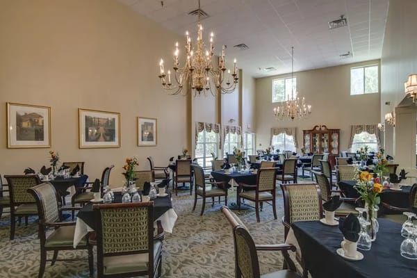 Elegant dining room with tables set for meals, featuring chandeliers and artwork
