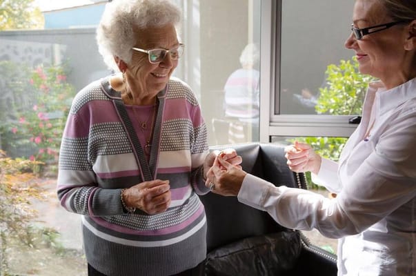 A smiling senior woman interacts with a staff member in a cozy indoor setting.