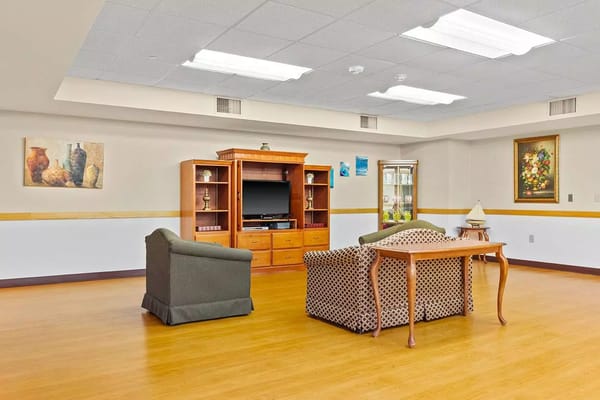 A living room with a green armchair, patterned couch, and wooden table.