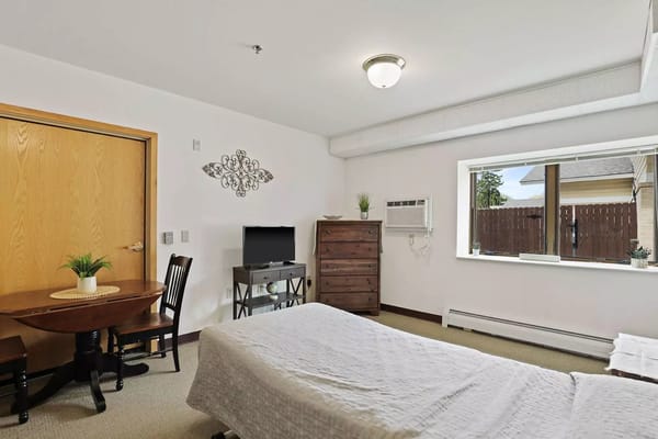 Bedroom featuring a bed, a TV, and a table in Sun Prairie Senior Living
