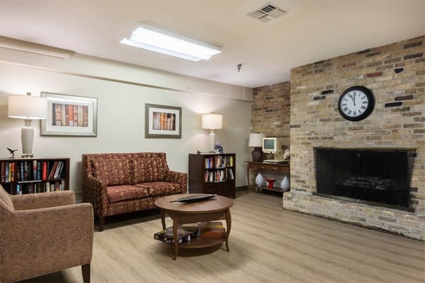 Cozy living room with seating and a fireplace at The Bay at Belmont Health and Rehabilitation Center.
