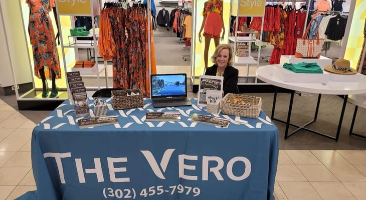 A staff member at The Vero information booth surrounded by promotional materials.