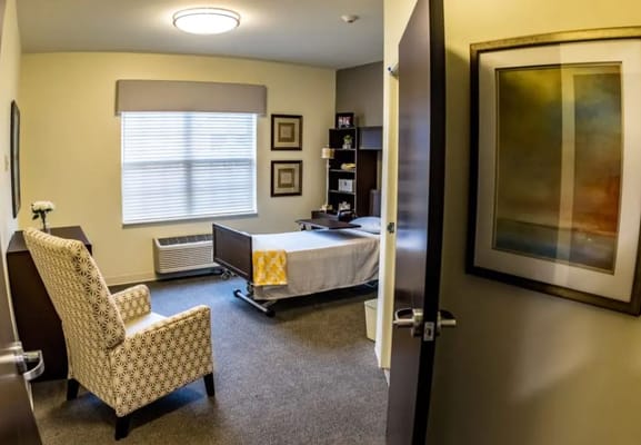 Private bedroom in a senior living facility featuring a bed, chair, and desk.