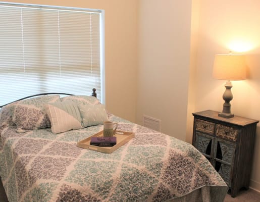 A well-decorated bedroom with a bed, bedside table, lamp, and window.
