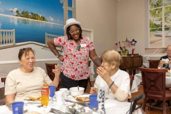 Residents enjoying a meal with attentive staff in a dining area