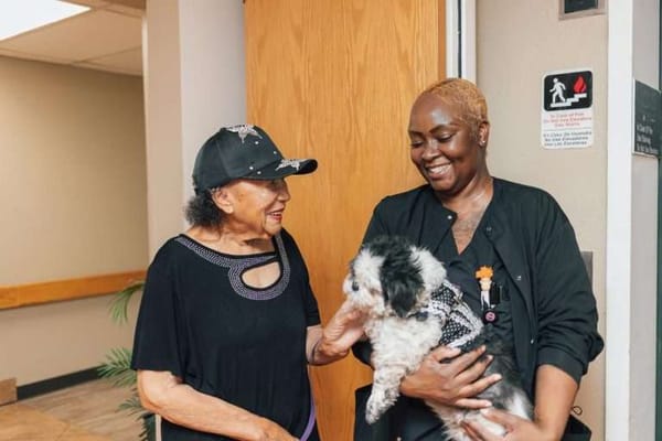 Two women smiling and interacting with a dog in a common area