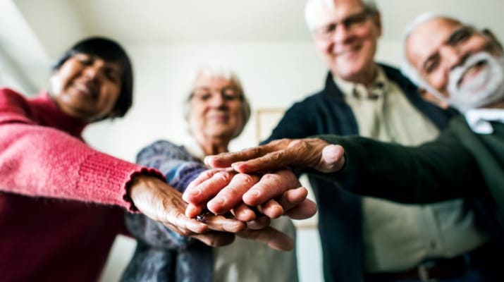 Four seniors smiling and placing their hands together
