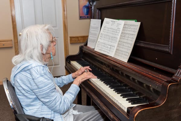 An elderly woman playing piano in a communal area