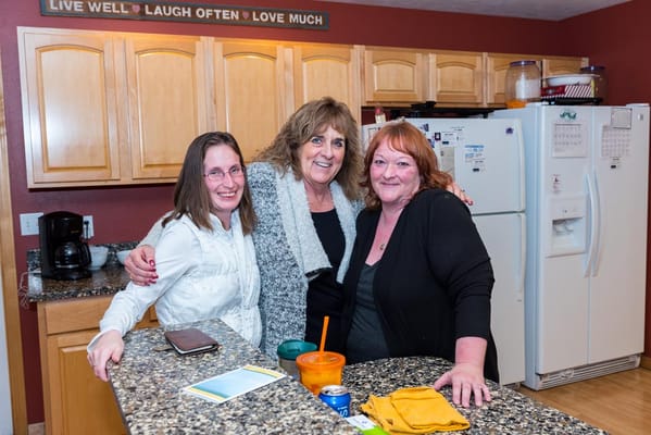 Three women smiling in a kitchen setting