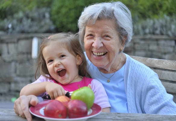 A joyful elderly woman and a girl sharing apples outdoors