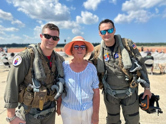 A woman poses with two military pilots outdoors