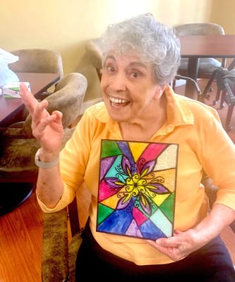 A smiling resident holding a colorful art piece in an activity room