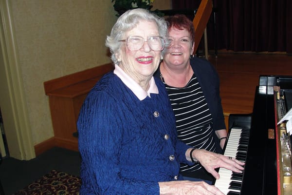Resident and staff member smiling at a piano