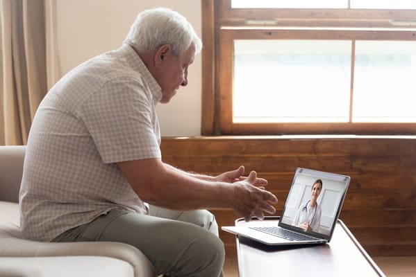 An older man in a virtual consultation with a nurse on laptop