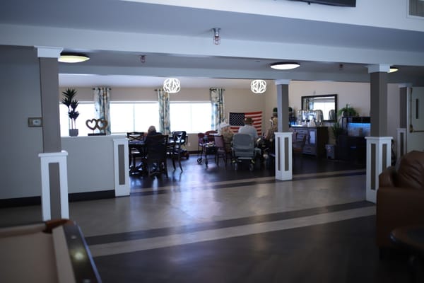 Common area with residents seated at tables and an American flag visible