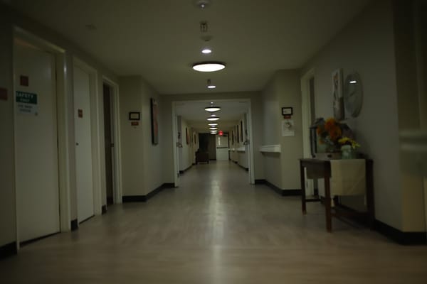 A hallway in Sterling Ridge Senior Living facility with doors on either side and a sitting area visible in the distance.