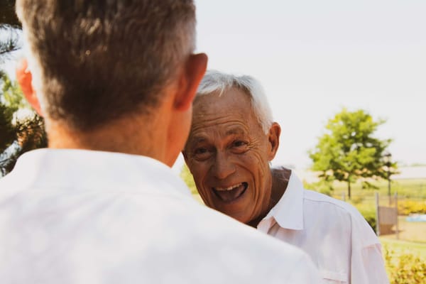 Two elderly men conversing outdoors, smiling