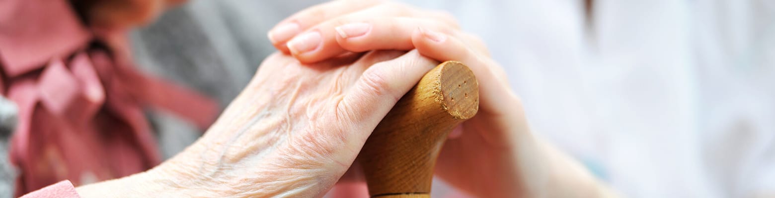 Two elderly hands holding a cane together