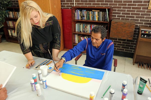 Resident painting with staff assistance in an activity room