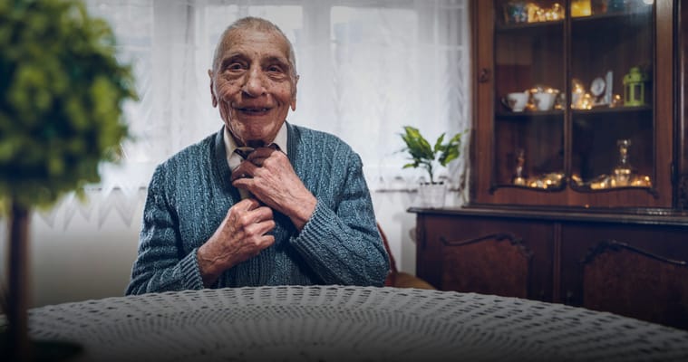 Elderly man smiling and adjusting his tie indoors