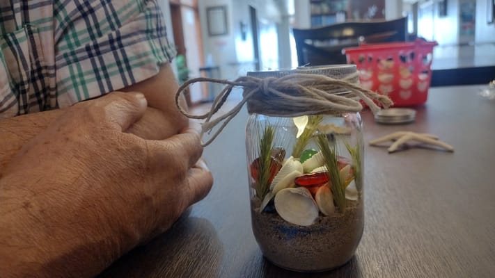 A resident's hands creating a decorative jar with shells