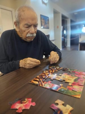 An elderly man working on a puzzle in a common area