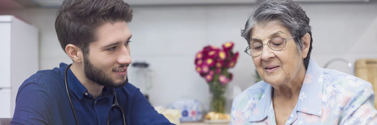 A caregiver interacting with an elderly woman in a kitchen setting