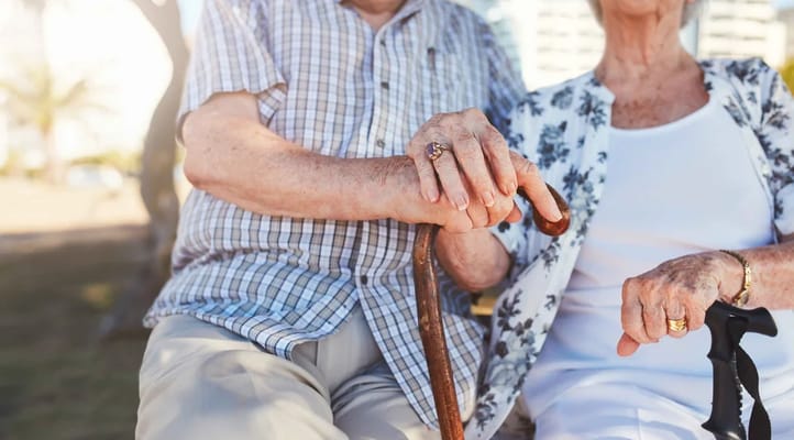 Two seniors holding hands, sitting outdoors.