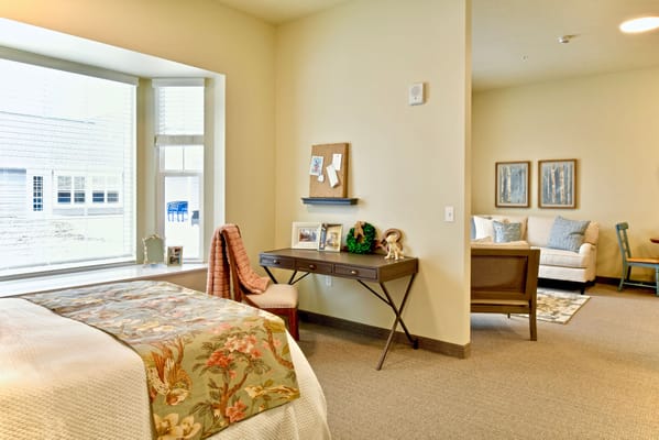 Well-decorated bedroom in senior living facility with desk and seating area