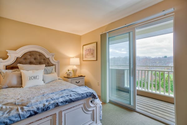 A well-decorated bedroom with a balcony, featuring a bed with decorative pillows and a lamp.