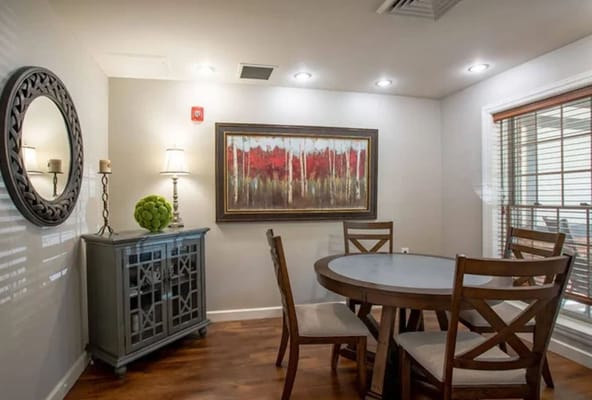 A cozy dining area with a round table and chairs, featuring a decorative painting and a mirror.