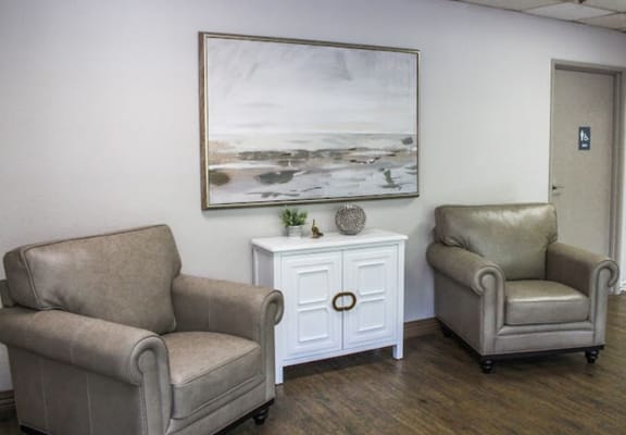 Two beige armchairs in a cozy living area with a painting and decorative items.