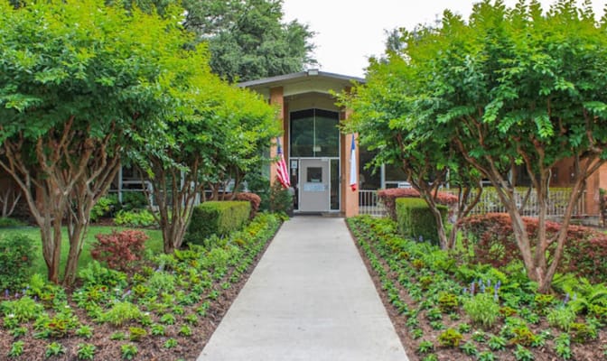Entrance pathway lined with greenery and flags at Diversicare of Lake Highlands