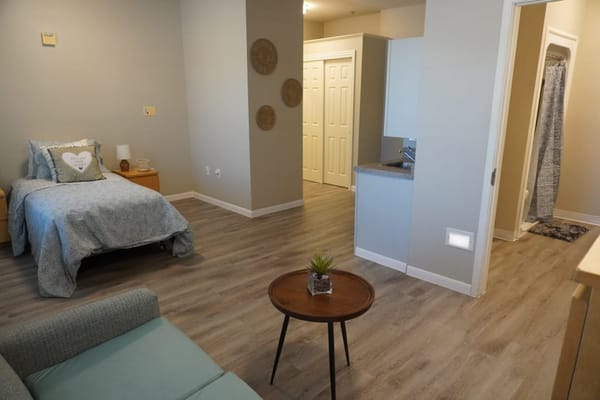 A cozy furnished resident room with a bed and small table