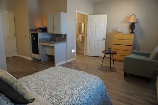 A cozy resident room with a bed, dresser, and seating