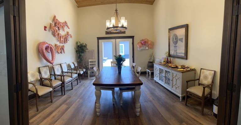 Interior view of the gathering room decorated for an event with a long table, chairs, and balloons.