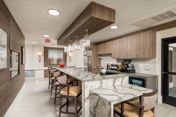 A spacious bar area with a marble counter and seating in a senior living facility.