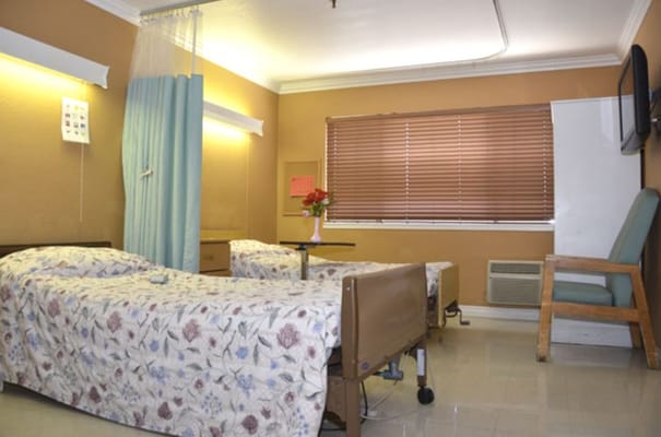 A spacious bedroom with two beds, a bedside table, and natural light from a window.