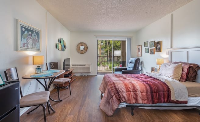 A well-furnished bedroom with a sleeping area, a small dining table, and a balcony view.