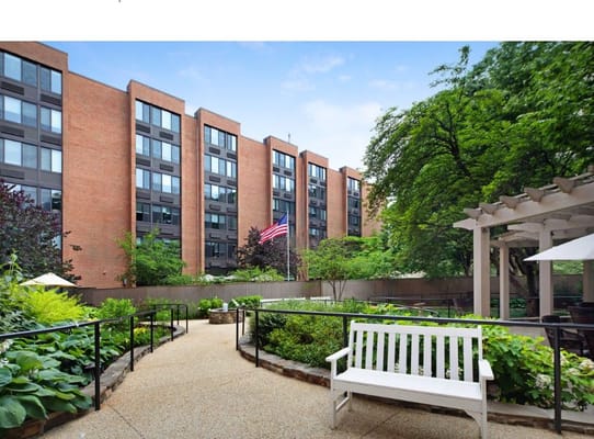 View of the garden area at Sunrise of Montgomery Village with a bench and greenery.