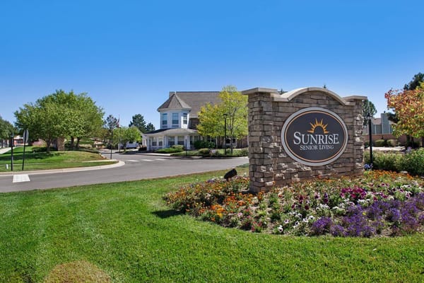 Sign for Sunrise Senior Living surrounded by flowers and greenery.