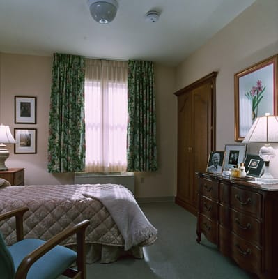 A well-furnished bedroom with a bed, dresser, and window with floral curtains.